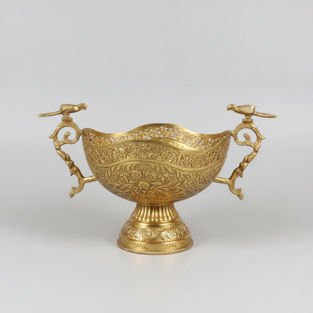 An ornate gold-toned metal serving bowl with intricate embossed floral patterns and decorative handles, displayed on a dark marble table in what appears to be a shop or showroom.