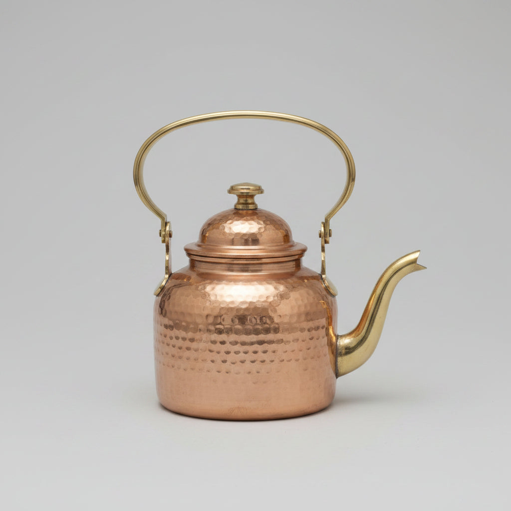 Copper teapot with gold handle and spout on a reflective surface