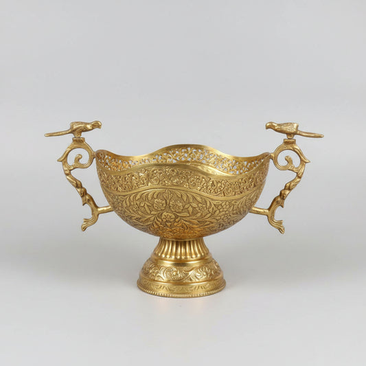 An ornate gold-toned metal serving bowl with intricate embossed floral patterns and decorative handles, displayed on a dark marble table in what appears to be a shop or showroom.