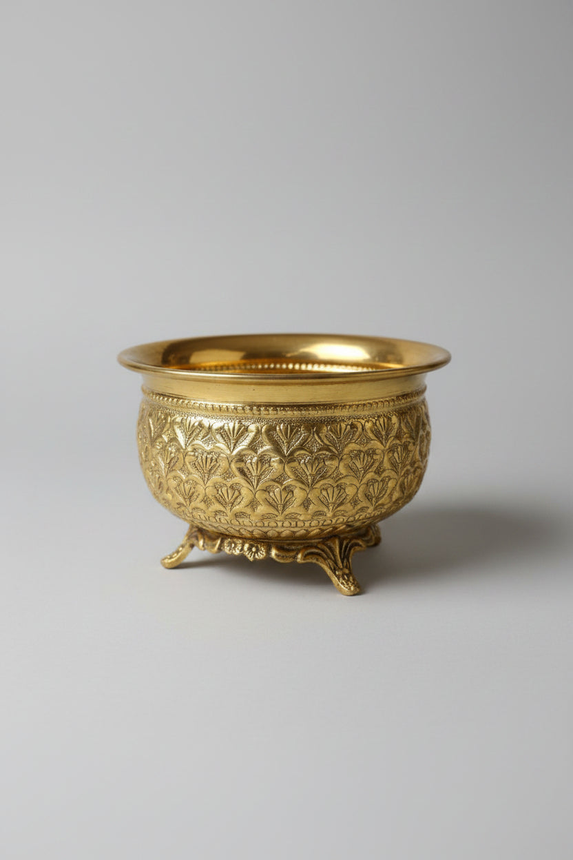 An ornate gold-colored metal incense burner with intricate floral relief patterns and three feet, displayed on a dark marble surface.