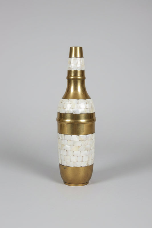 Decorative bottle with brass and shell inlay on a reflective surface