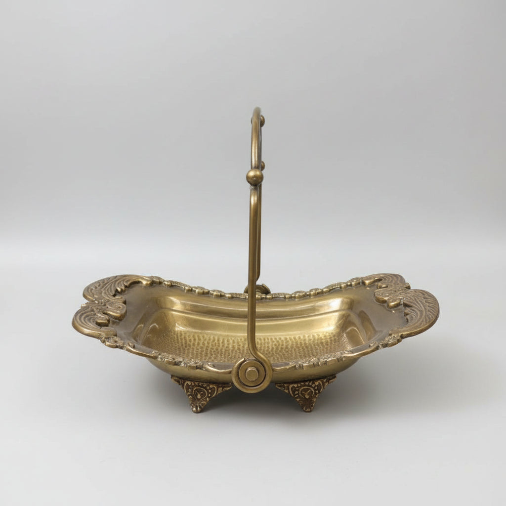 An ornate brass serving basket with a high handle, placed on a dark marble table inside what appears to be a shop or showroom.