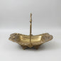 An ornate brass serving basket with a high handle, placed on a dark marble table inside what appears to be a shop or showroom.