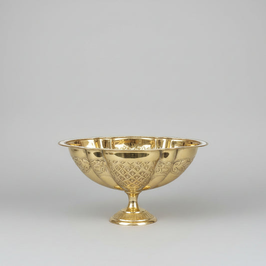 A shiny gold pedestal bowl with a cut crystal pattern, displayed on a reflective marble counter inside what appears to be a shop or showroom.