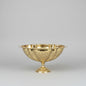 A shiny gold pedestal bowl with a cut crystal pattern, displayed on a reflective marble counter inside what appears to be a shop or showroom.