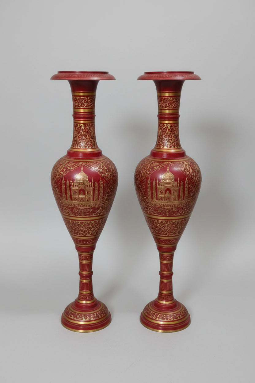 Two ornate red and gold vases on a reflective surface with a blurred background.