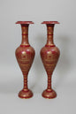 Two ornate red and gold vases on a reflective surface with a blurred background.