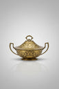 An ornate brass tureen with a lid, featuring embossed floral patterns and side handles, displayed on a glass-topped table inside what appears to be a shop.