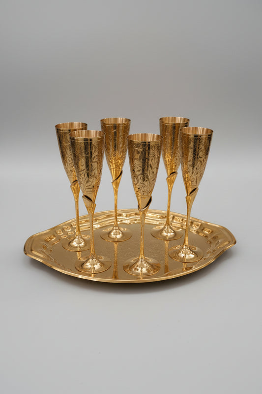 Set of gold champagne flutes on a matching tray on a white tablecloth.
