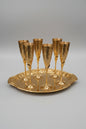 Set of gold champagne flutes on a matching tray on a white tablecloth.